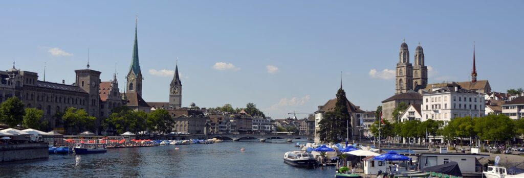 Explore Zurich's historic cityscape along the waterfront with iconic churches and bustling activity.