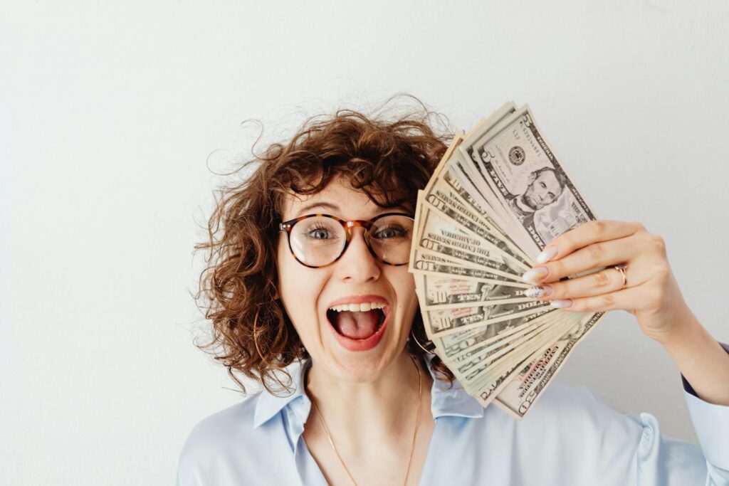 Caucasian woman with curly hair delights in holding US dollars against a white background.