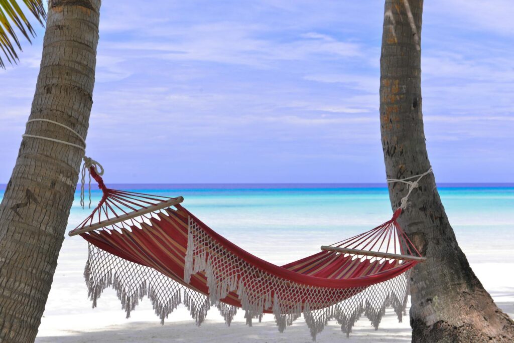 Idyllic beach hammock between coconut trees with azure blue waters.