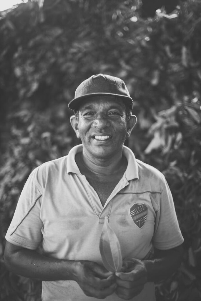 Portrait of a smiling Sri Lankan farmer in a polo shirt holding a leaf outdoors.